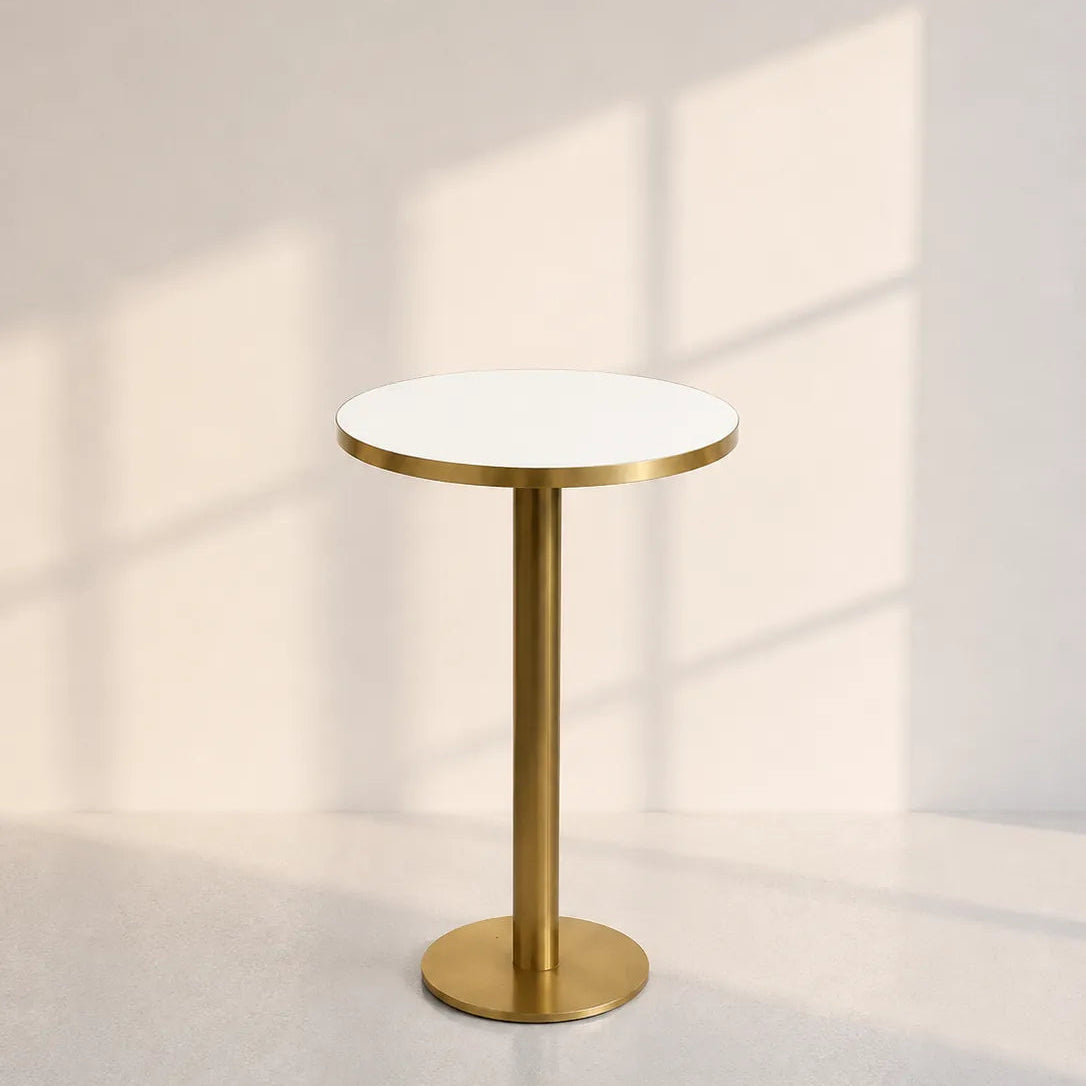 Image of A modern round side table with a white tabletop and a brushed gold metal pedestal base, set against a warm beige wall with soft window shadow patterns.