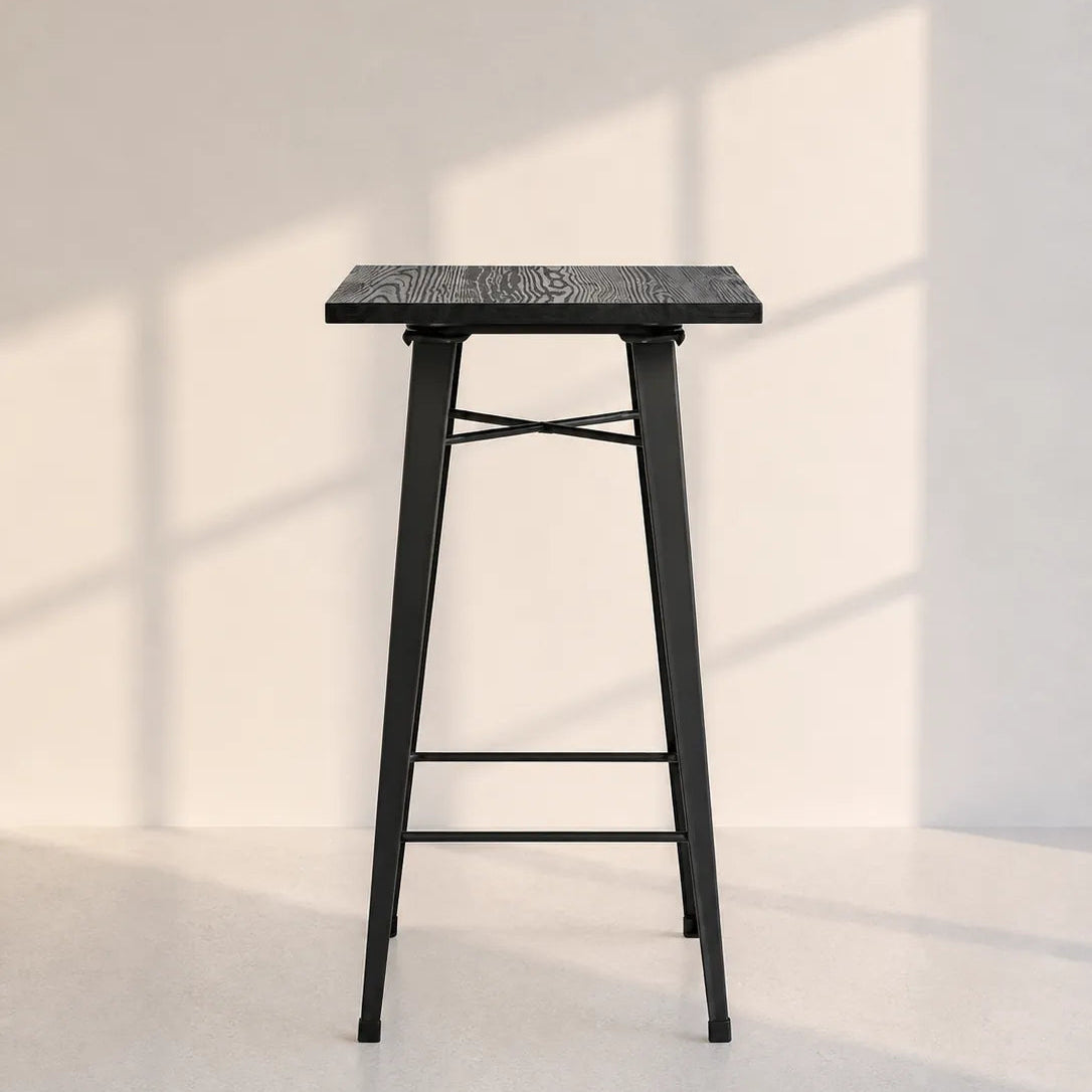 Image of A modern black metal bar stool with a textured square seat and a lower support rail, set against a minimalist off-white wall with soft window shadow patterns.