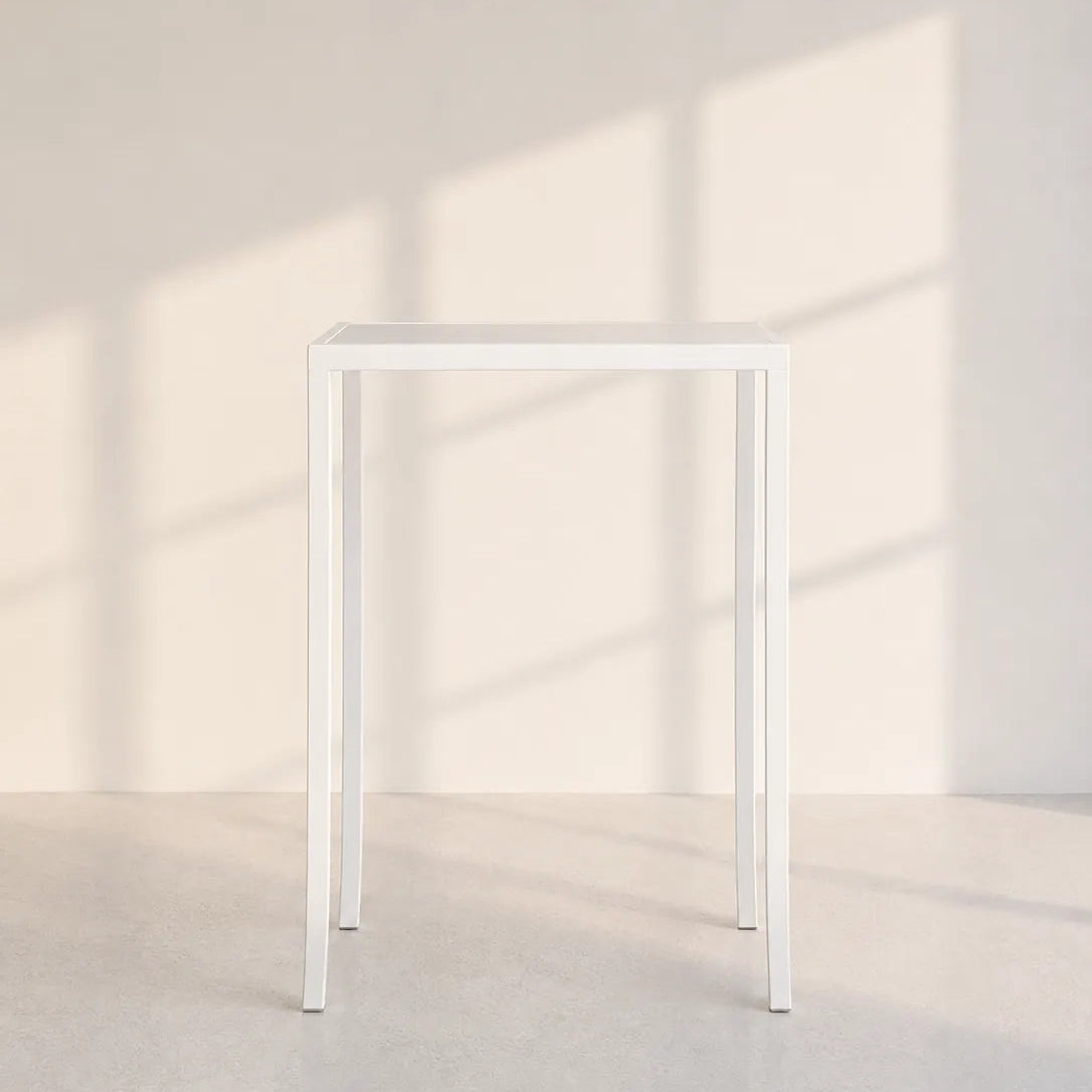 A minimalist white metal console table with a square top and four slim legs, set against a warm beige wall with soft window shadow patterns.