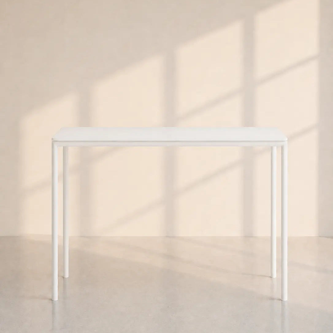 Image of A minimalist white rectangular table with slim legs, positioned against a warm beige wall with soft window shadow patterns.