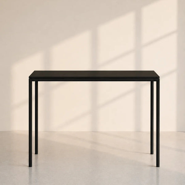 A minimalist black metal console table with a rectangular top and slim legs, set against a warm beige wall with soft window shadow patterns.