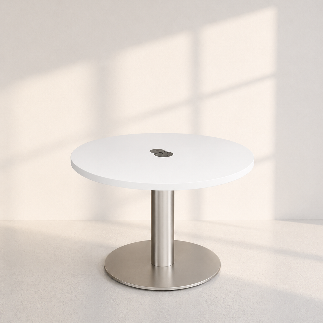 A minimalist round white table with a brushed silver metal pedestal base, set against a warm off-white wall with soft window shadow patterns.