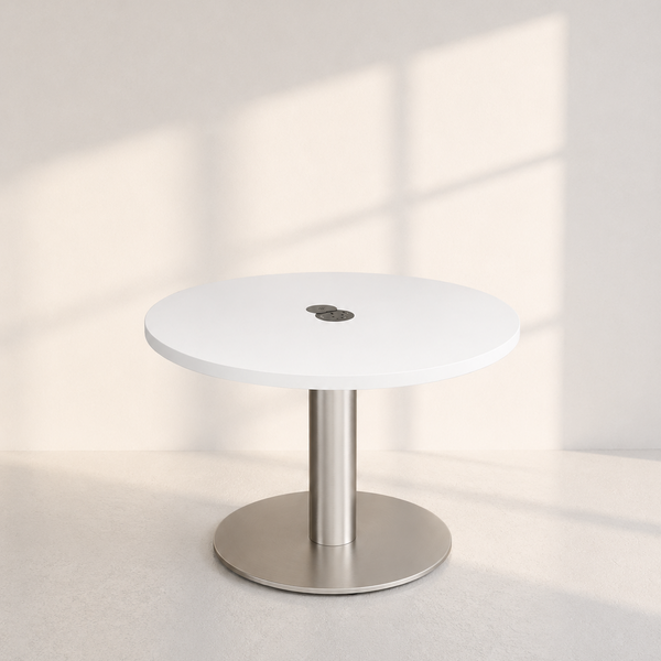 A minimalist round white table with a brushed silver metal pedestal base, set against a warm off-white wall with soft window shadow patterns.