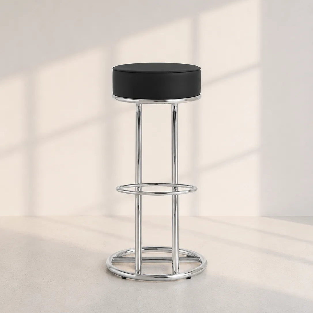 Image of A modern bar stool with a round black upholstered seat and a polished chrome metal frame, set against a minimalist off-white wall with soft window shadow patterns.