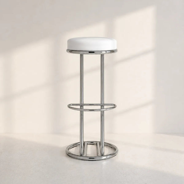 A modern bar stool with a white circular cushioned seat and a polished chrome metal frame, set against a minimalist off-white background with soft window shadow projections.