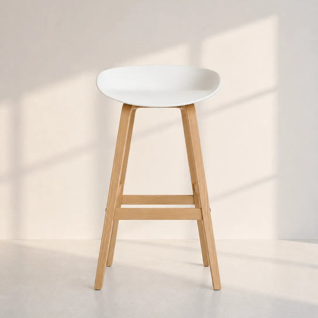 Image of A modern bar stool with a white molded seat and light natural wood legs, set against a minimalist beige wall with soft window shadow patterns.