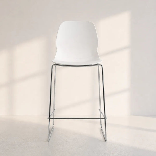 A modern white bar stool with a molded plastic seat and slim chrome metal legs, set against a minimalist off-white wall with soft window shadow patterns.
