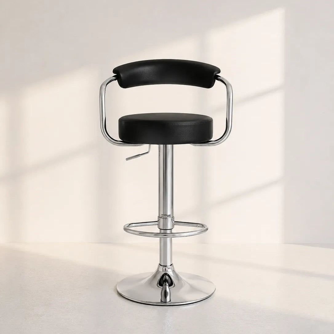 Image of A modern bar stool with a black faux-leather seat and backrest, supported by a polished chrome metal frame, footrest, and circular base, set against a minimalist off-white wall with soft window light shadows.