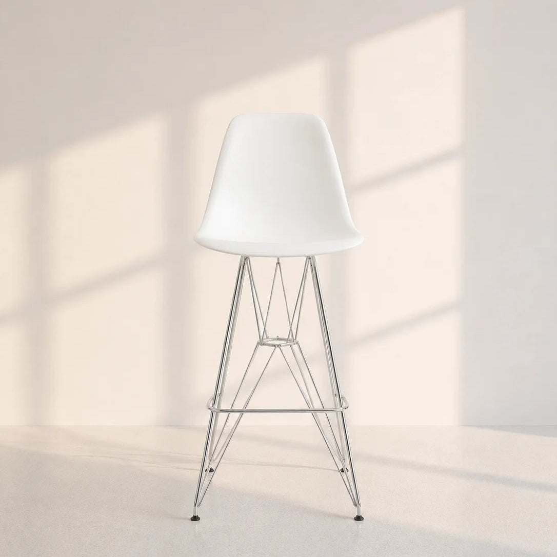 A modern white molded plastic bar stool with a chrome wire frame, set against a minimalist beige wall and floor with soft window shadow patterns.