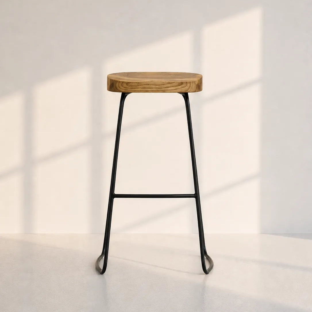 Image of A modern bar stool with a round natural wood seat and a black metal frame, set against a minimalist off-white wall with soft window shadow patterns.
