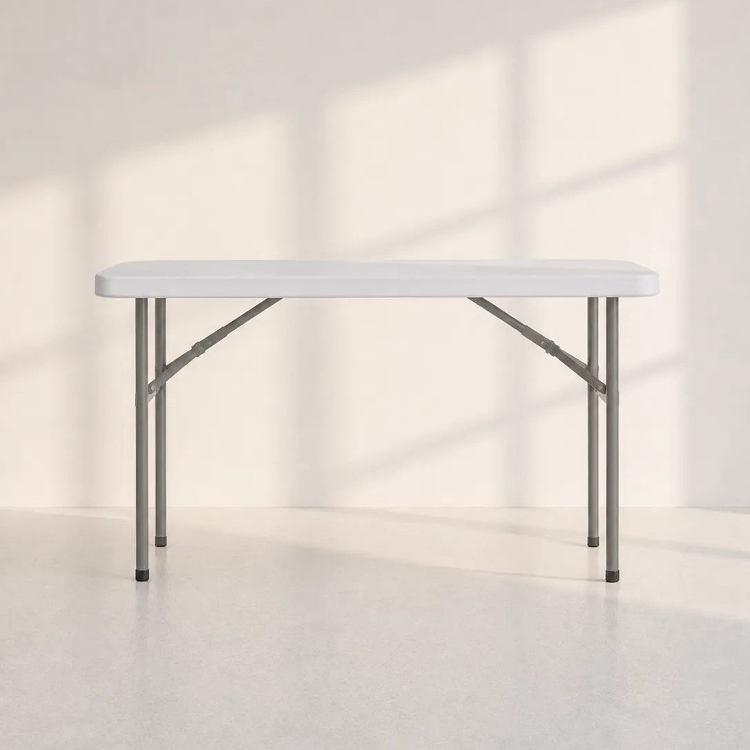 Image of A white rectangular folding table with gray metal legs, shown in a minimalist studio setting with soft window shadow patterns on a light beige wall and floor.