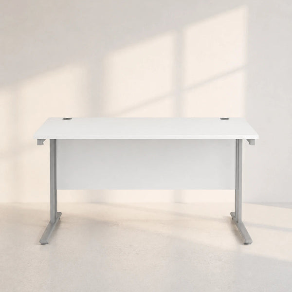 A modern white desk with a white desktop and gray metal legs, positioned against a minimalist off-white wall with soft window shadows.