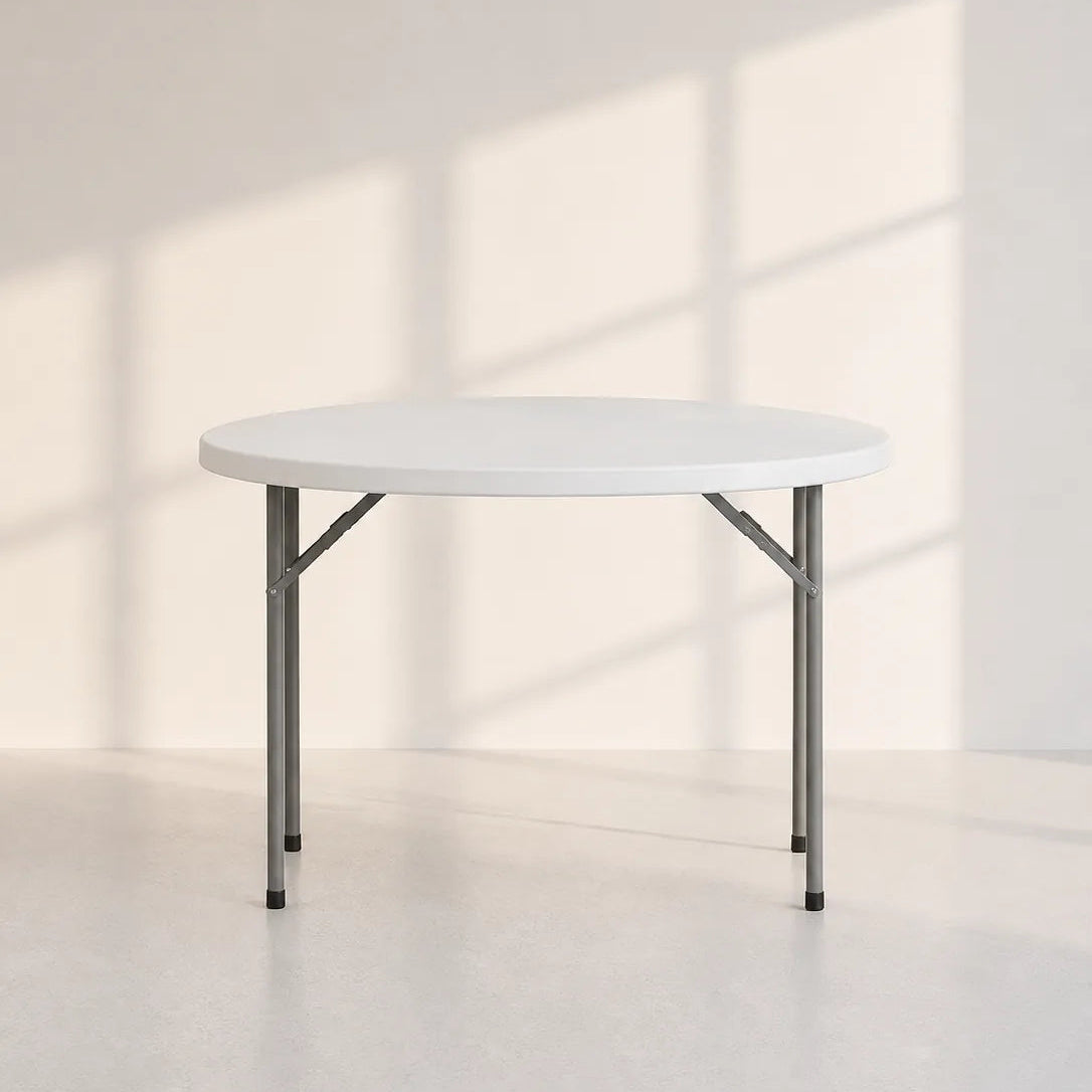 Image of A round folding table with a white top and gray metal legs, set against a minimalist off-white wall with soft window shadow patterns.