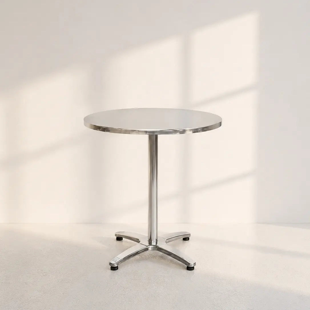 Image of A round metal pedestal table with a chrome star base, photographed in a minimalist studio setting with soft window-box shadows on a light wall and floor.