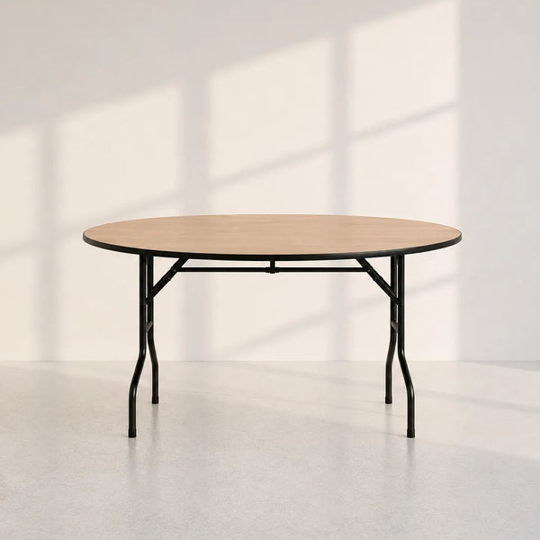 A round folding table with a light natural wood top and black metal legs, set against a minimalist off-white wall with soft window shadow patterns.