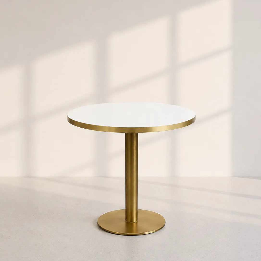 Image of A modern round side table with a white marble top and a brushed brass pedestal base, set against a minimalist beige wall with soft window shadow patterns.