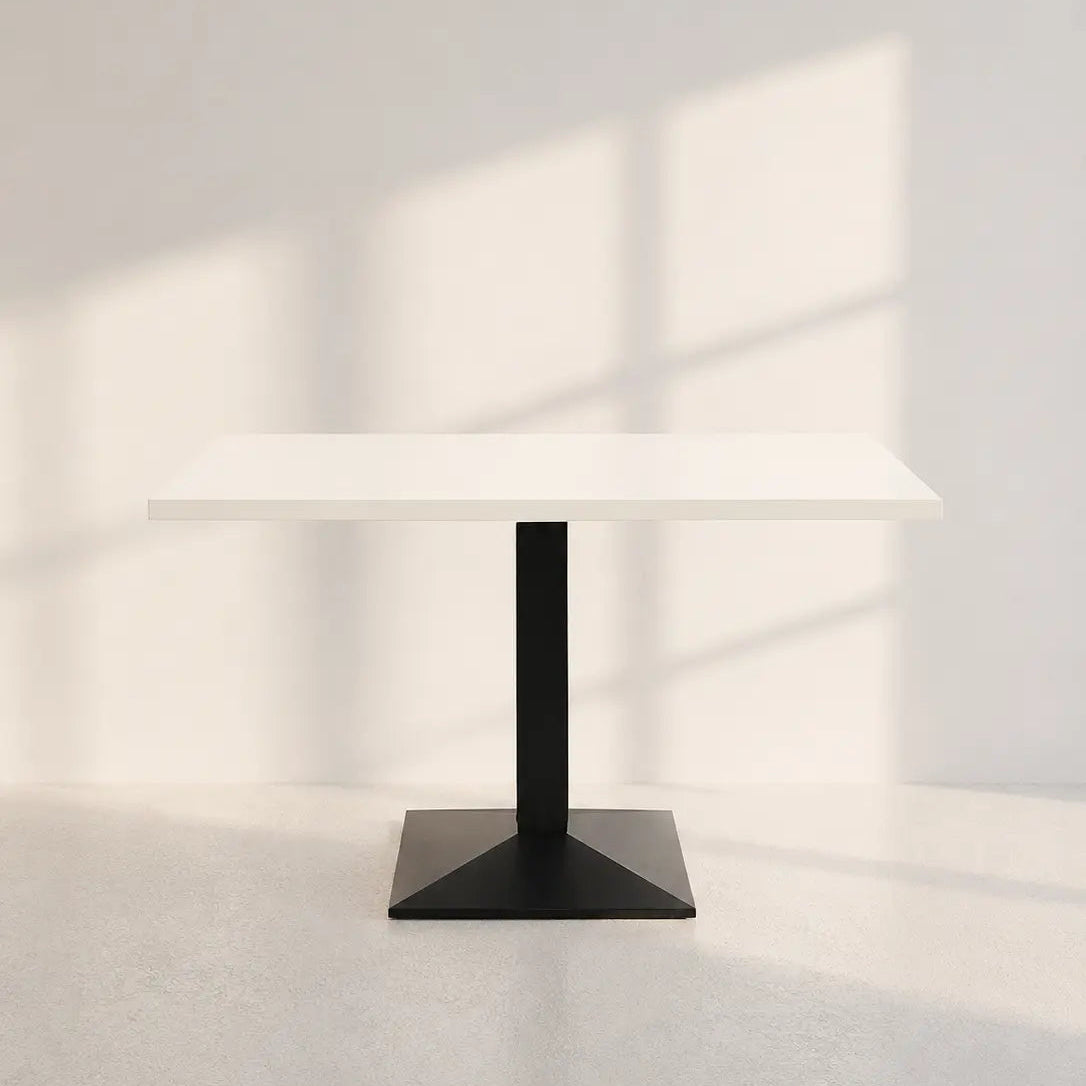 Image of A modern dining table with a white rectangular top and a black metal pedestal base, set against a minimalist white wall with soft window shadow patterns.